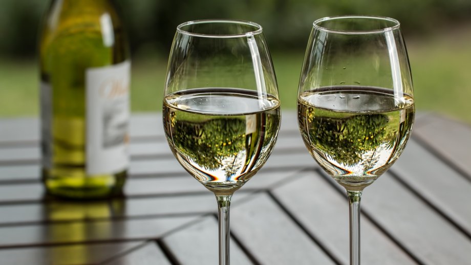 Zwei Gläser mit Weißwein stehen auf einem Tisch, im Hintergrund eine Flasche.