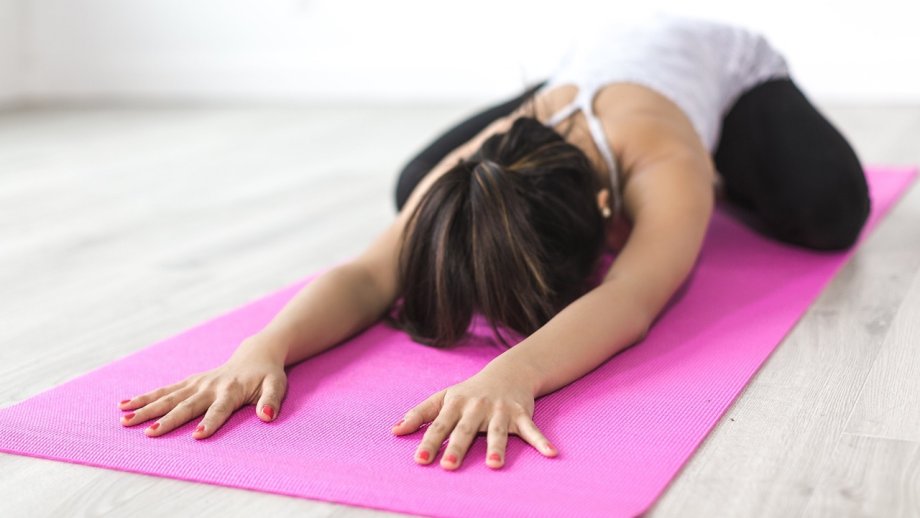 Frau liegt in einer entspannten Yoga-Position auf einer pinkfarbenen Matte