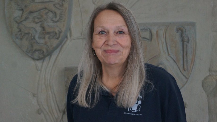 Eine Frau mit langen grauen Haaren vor eine steinernen Wand.