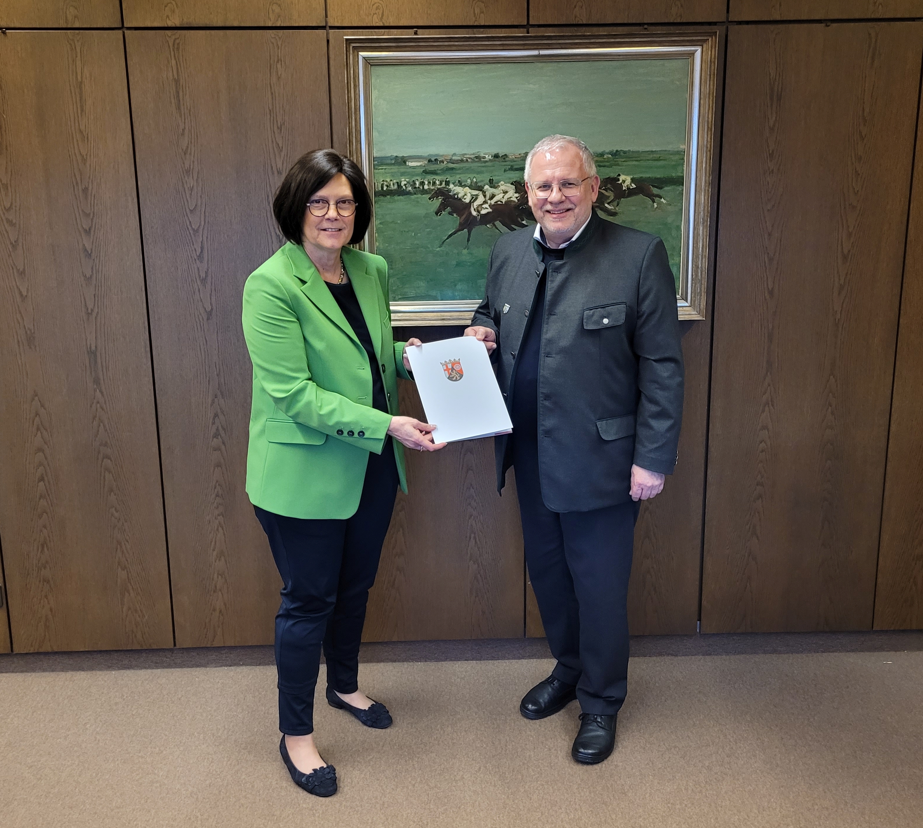 Eine Frau übergibt einem Mann eine Mappe. 