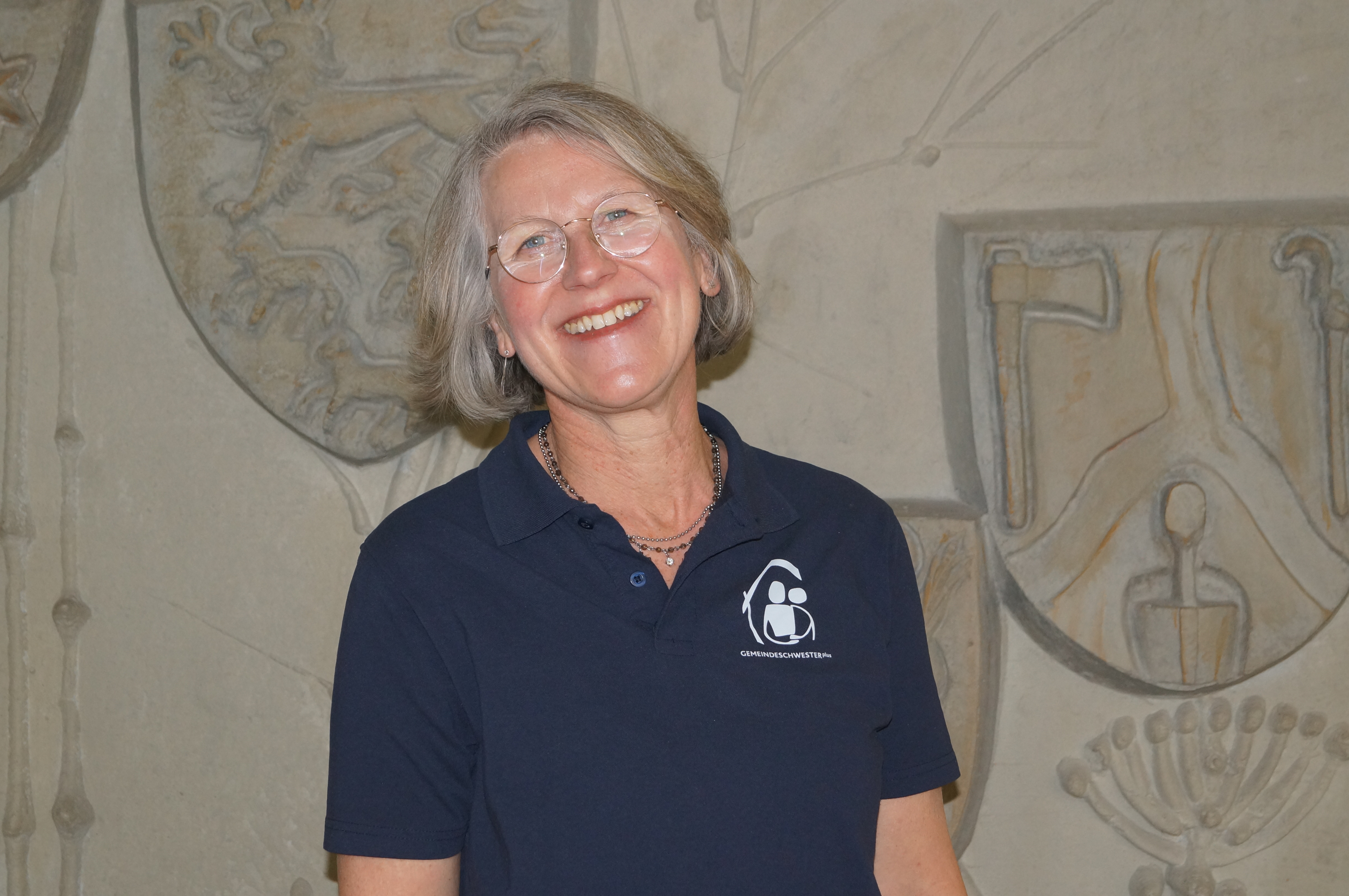 Vera Götz, eine Frau mit kinnlangen, grauen Haaren und Brille, lächelt in die Kamera. 