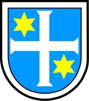 Wappen der Stadt Deidesheim. Ein weißes Kreuz auf hellblauem Grund mit einem gelben Stern in der Ecke links oben und der Rundung rechts unten. Weiße Umrahmung. 