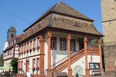Das historische Rathaus in Freinsheim. Ein weißes Gebäude mit Säulen und Umrahmungen der Fenster aus rotem Sandstein, einer Freitreppe mit Geländer aus rotem Sandstein.