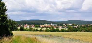 Blauer Himmel über dem Ort Hettenleidelheim. Im Vordergrund Felder und links ein Nadelbaum.