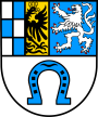 Wappen von Quirnheim. Untere Hälfte auf weiß ein nach unten offenes, blaues Hufeisen. Oben geteilt. Rechts ein weißer Löwe auf Hellblau. Links noch einmal geteilt. Ganz links blau-weiß kariert, daneben ein halber schwarzer Adler auf gelb. 
